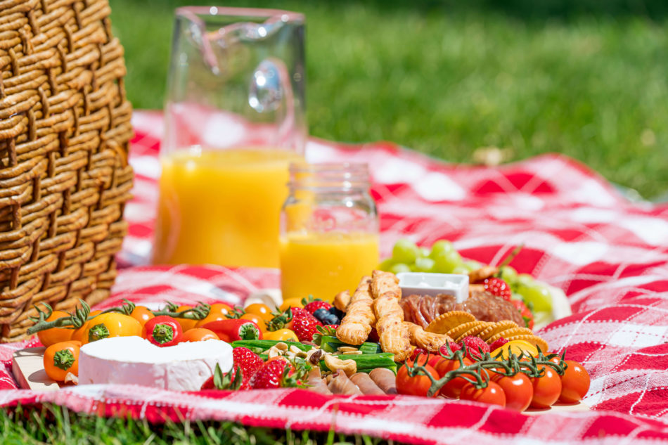 Cheese, vegetables and crackers on a picnic blanket next to a pitcher and mason jar filled with orange juice. 