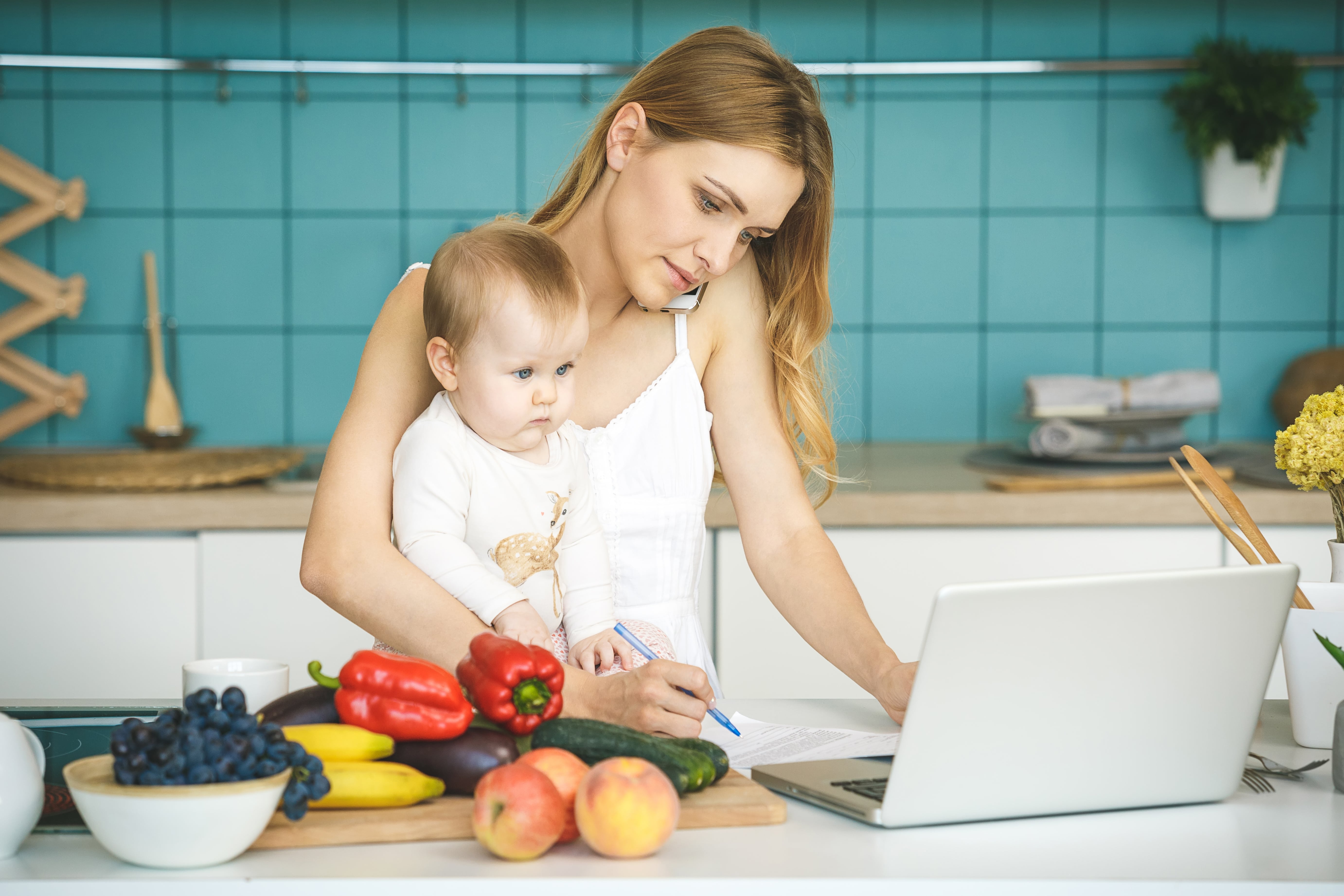 busy mom holding baby in kitchen while trying to prepare dinner